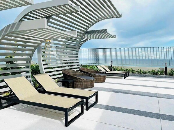 A rooftop terrace with lounge chairs, a pergola, and a view of the ocean. - The Song Apartment Vung Tau - RUBY HOUSE (Ho Chi Minh City)