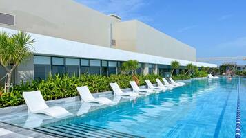 A swimming pool with lounge chairs, a building with large windows, and greenery.