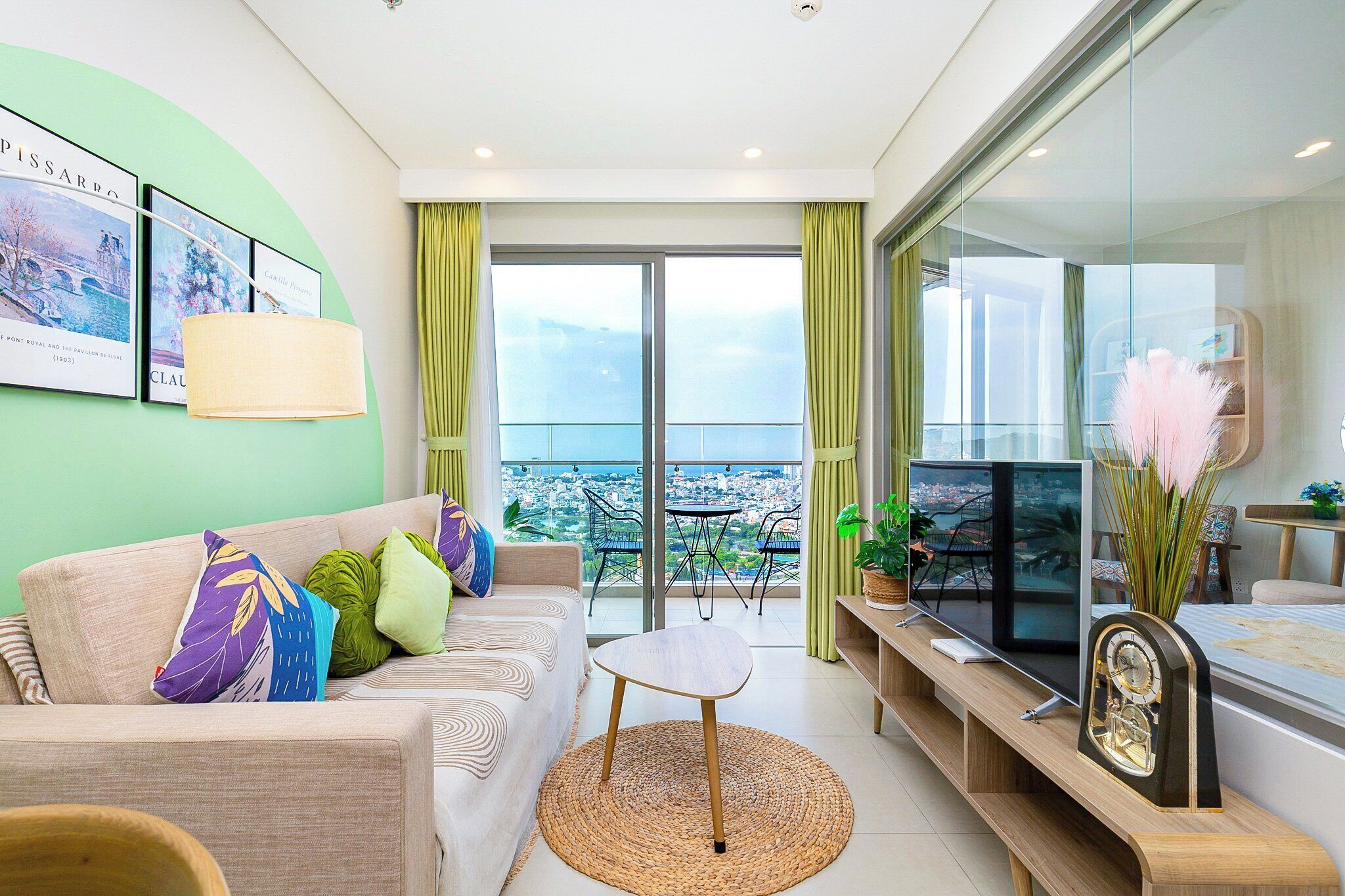 Un salon moderne avec un canapé, une petite table ronde, un téléviseur et un balcon offrant une vue sur la ville.