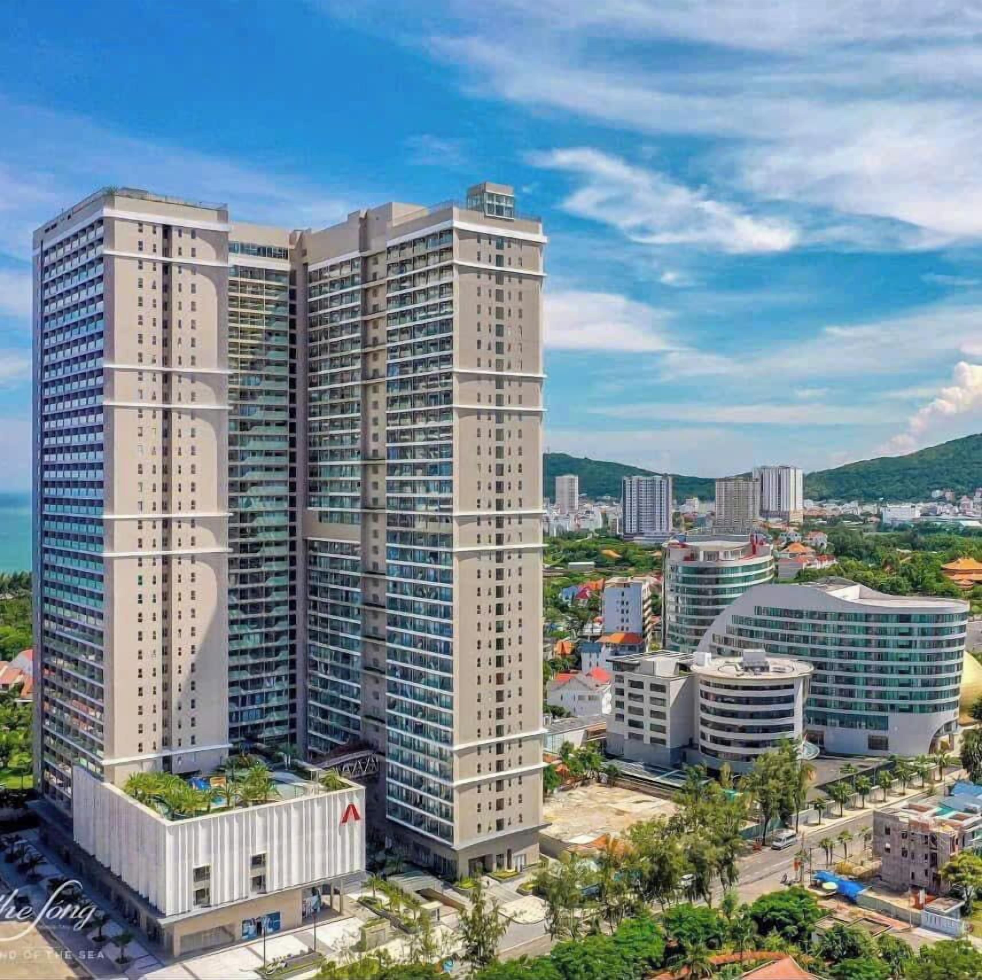 Un edificio alto con varios pisos, rodeado de otros edificios y vegetación.