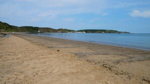 Ein sandiger Strand mit sanften Wellen, wolkenlosem Himmel und fernen Hügeln.