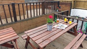 A wooden deck with picnic tables, a potted plant, and a bottle of beer. - 2 Bed in Tresaith (oc-26679) (Tresaith)