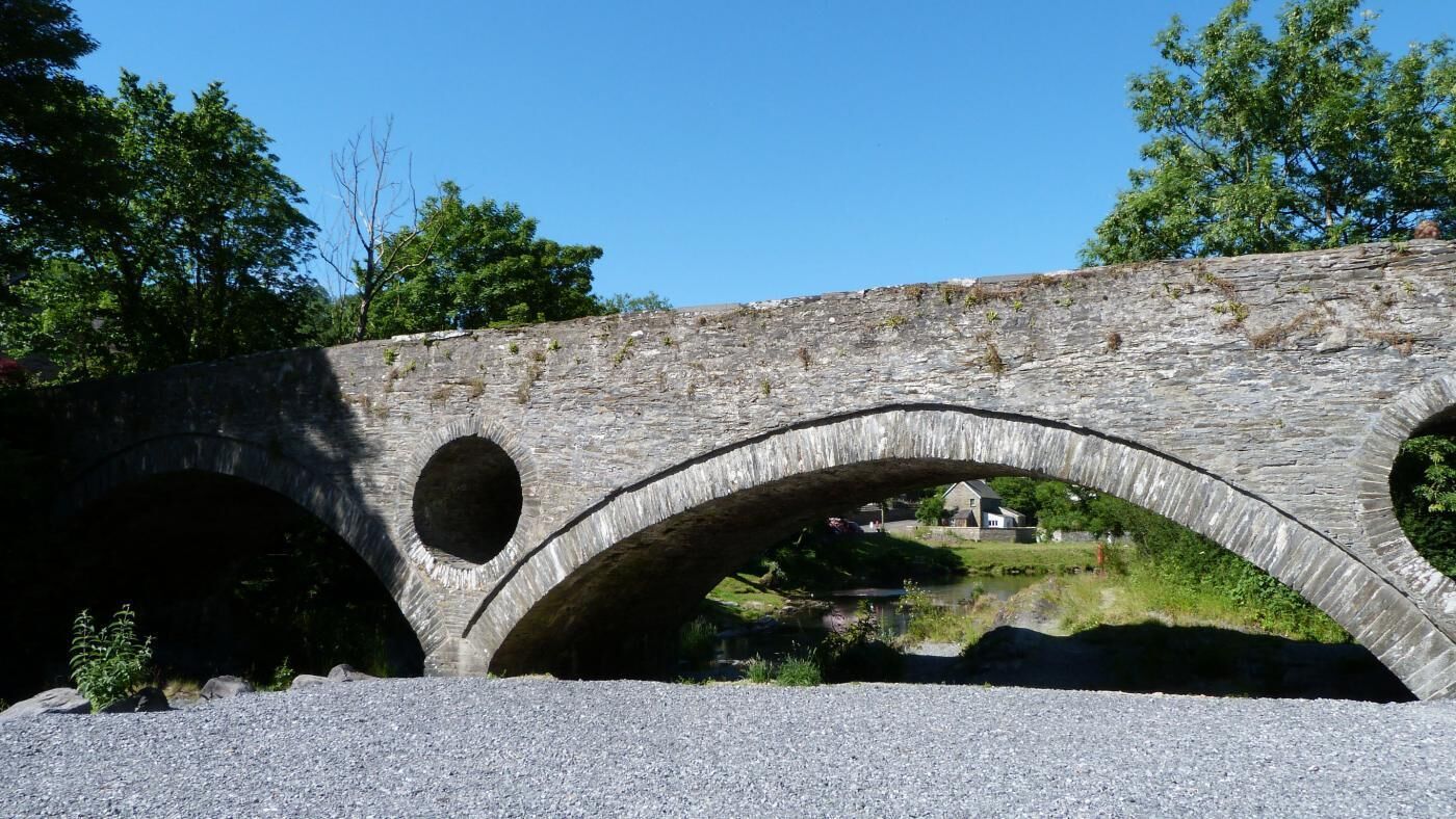 Un ponte in pietra con tre arcate che sovrasta un fiume, circondato da vegetazione e alberi.