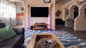 Een woonkamer met een flatscreen televisie, een bank, een salontafel en een kamerkleed met dessin.