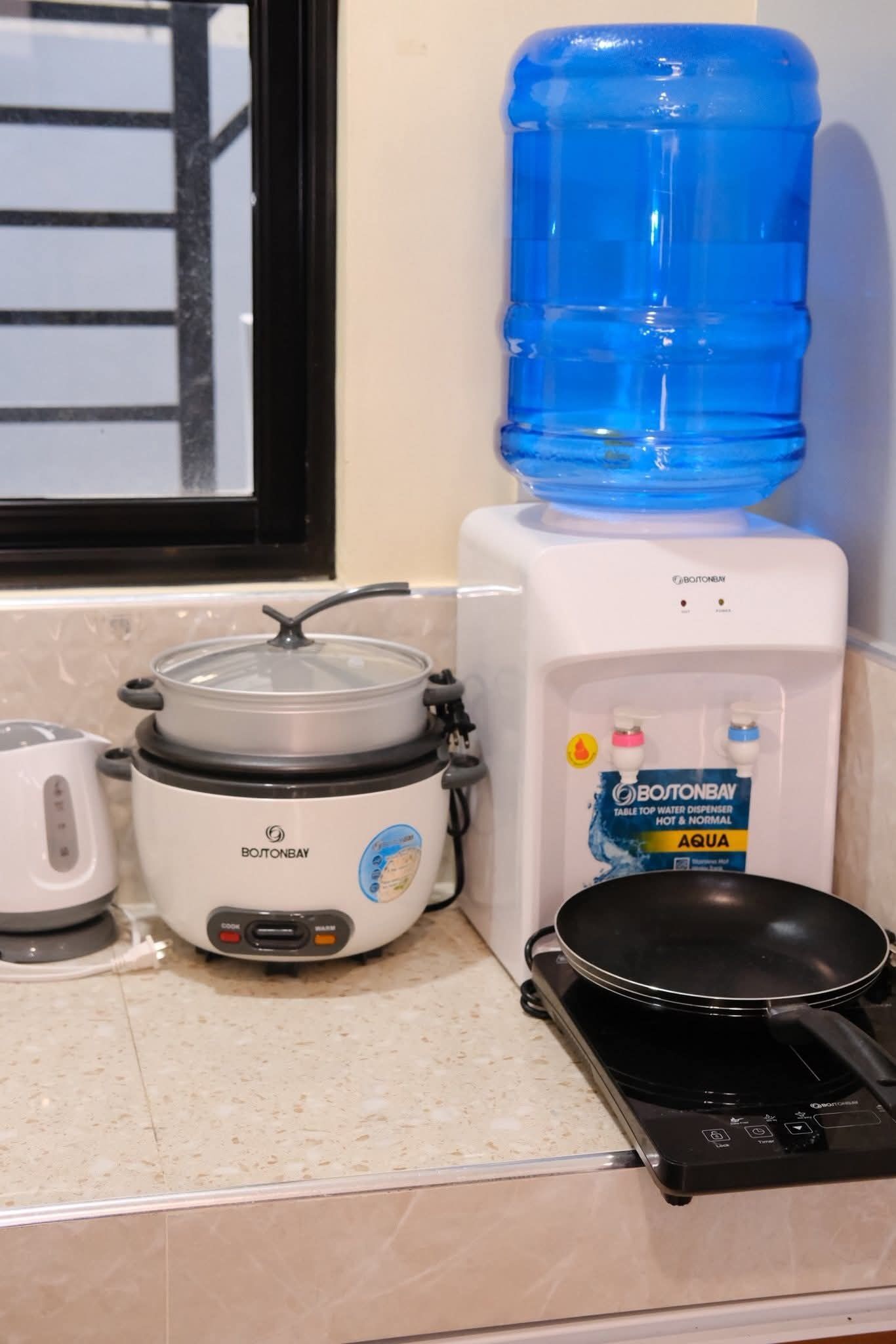 A kitchen with a stovetop, a slow cooker, a water dispenser, and a kettle.