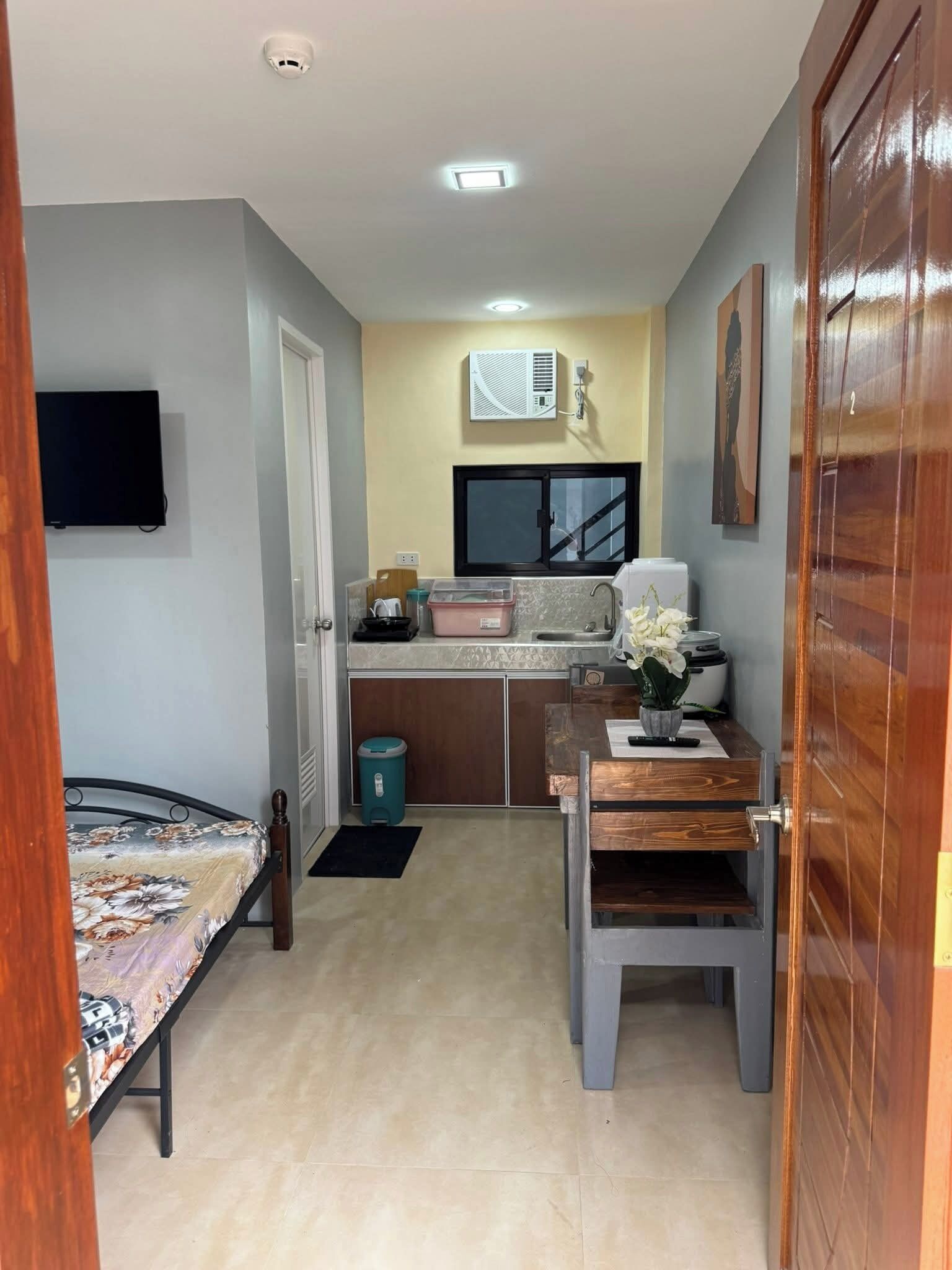 Une petite chambre comprenant un lit, une kitchenette, une télévision et une fenêtre.