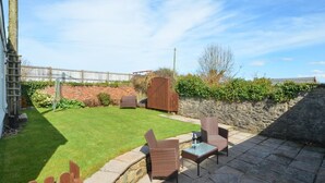 Un jardin avec une pelouse verdoyante, un mur de pierres, une clôture en bois et du mobilier d’extérieur.