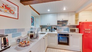 Une cuisine moderne avec des meubles blancs, un réfrigérateur rouge, un four à micro-ondes et un grille-pain.