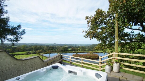A hot tub with a view of a lake and surrounding greenery. - 2 Bed in New Quay (oc-25595) (Mydroilyn)