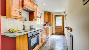 A kitchen with wooden cabinets, a built-in oven, a microwave, and a fruit bowl on the counter. - 2 Bed in New Quay (oc-25595) (Mydroilyn)