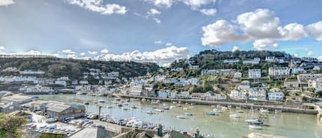 Un pueblo costero con un puerto deportivo, edificios a lo largo del litoral y una colina al fondo.