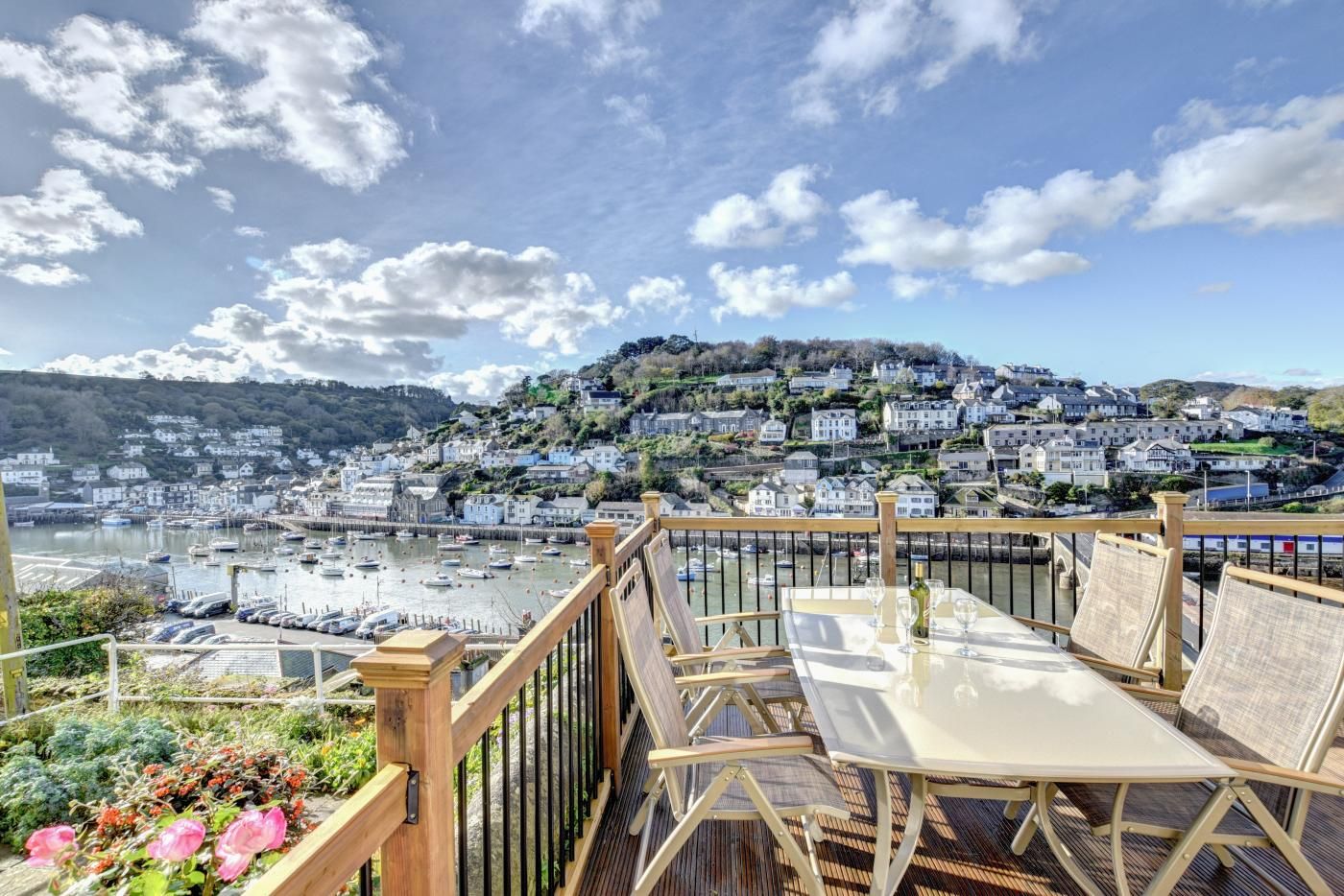 Une terrasse avec une table et des chaises donnant sur un port où sont amarrés des bateaux, ainsi que sur une ville située sur une colline.