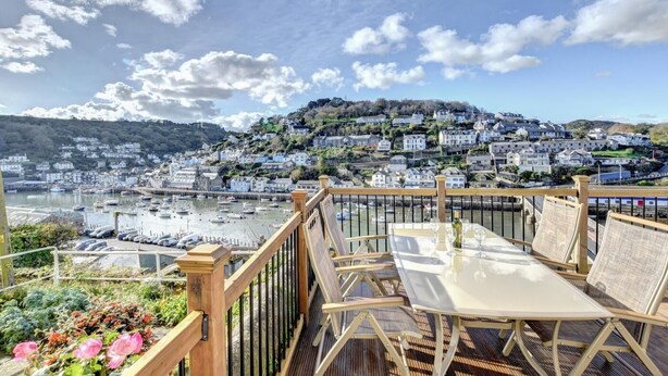 Una terraza con mesa y sillas que da a un puerto con barcos y un pueblo en la ladera.