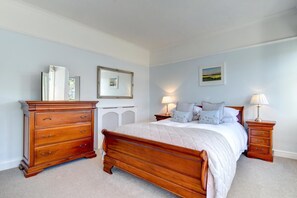 A bedroom with a wooden bed, a dresser, a radiator, and two bedside lamps. - 4 Bed in Looe (oc-l30049) (Looe)