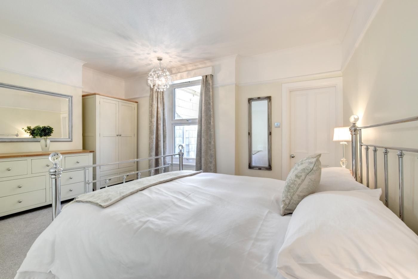 A bedroom with a large bed, a dresser, a mirror, and a chandelier.