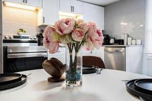 A modern kitchen with white cabinets, a stainless steel oven, and a vase with pink flowers on the counter. - Pelican Perch- 2BR Upstairs Unit- Short Walk To Beach- Firepit (North Myrtle Beach)
