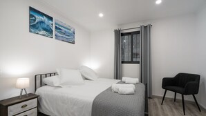 Et moderne soveværelse med seng, sengebord, lampe og stol.