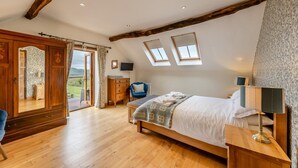 Una camera da letto con un letto grande, pavimento in legno, un armadio, una scrivania, una sedia e vista sull'esterno.