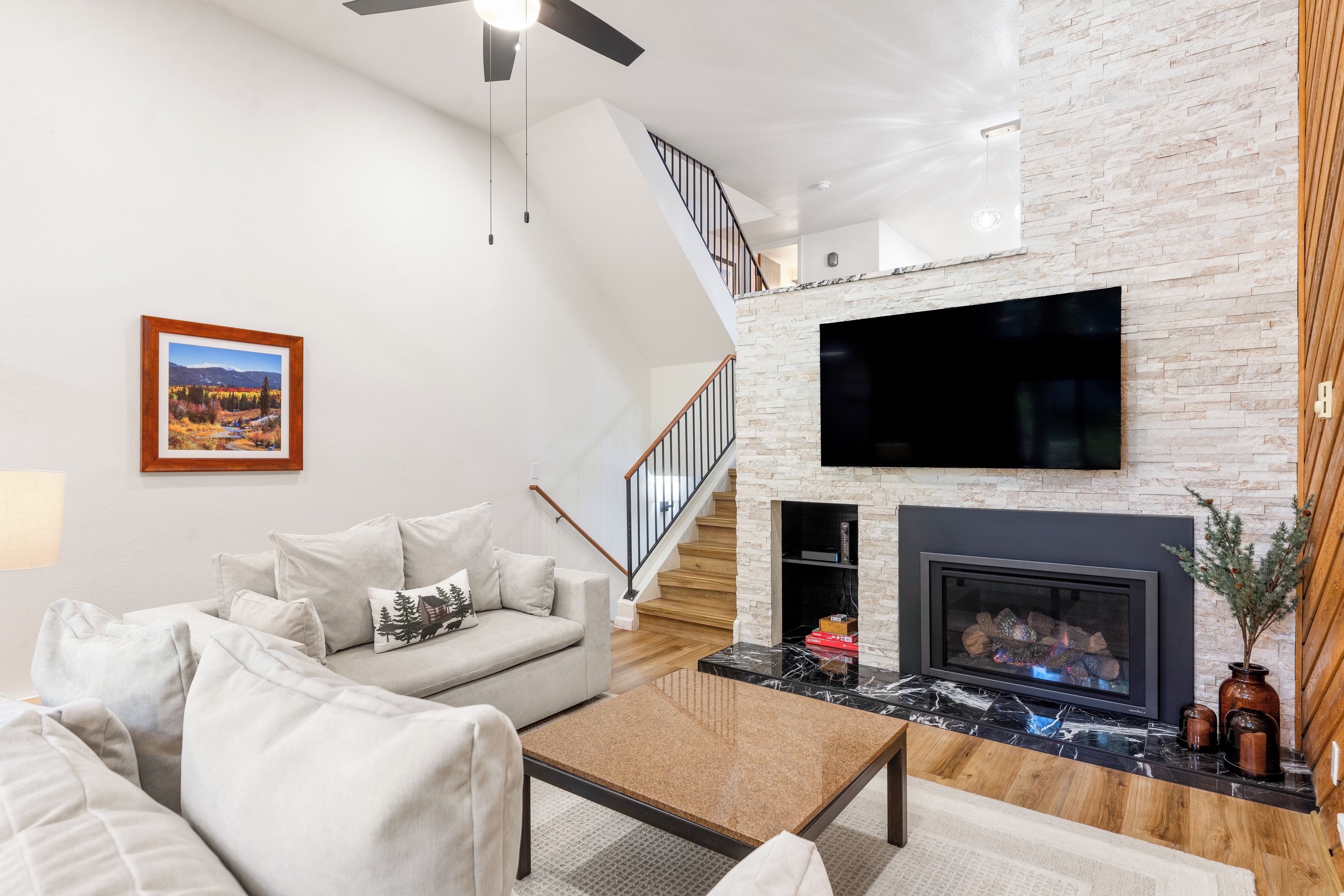 Un salon moderne avec un canapé, une table basse, une cheminée et un téléviseur fixé sur un mur en pierre.