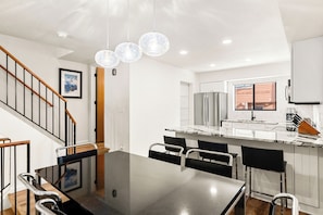 A modern kitchen with a marble countertop, stainless steel appliances, and a dining area with a glass table and black chairs. - Newly Remodeled; Great Location; Heated Garage (Breckenridge)