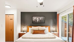 Moderni hotellihuone, jossa on suuri sänky, oma sisäänkäynti, kehystetty hirvikuvataulu ja näkymä ulos.