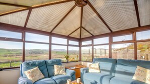 Ein Wintergarten mit Blick auf die Landschaft, ausgestattet mit zwei Sofas und einem kleinen Tisch.