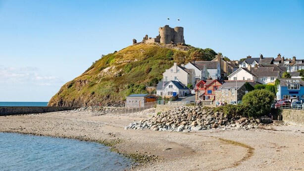 Eine Küstenstadt mit einer historischen Burg auf einem Hügel, einem Kiesstrand und Wohnhäusern.