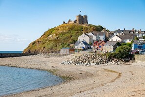 A coastal town with a historic castle on a hill, a pebble beach, and residential buildings. - 4 Bed in Morfa Bychan (oc-520440) (Porthmadog)