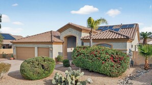 A residential house with a garage, solar panels, and a well-maintained garden with cacti and flowering plants. - Private Heated pool & Hot tub Oasis! (Goodyear)