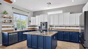 A modern kitchen with blue cabinets, a granite countertop, and stainless steel appliances. - Private Heated pool & Hot tub Oasis! (Goodyear)