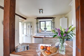 Een keuken met een houten tafel, een raam met gordijnen en een vaas met bloemen.