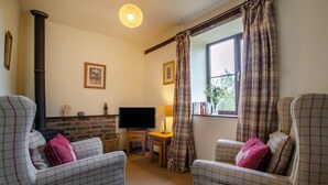 A cozy living room with two plaid armchairs, a television, a small table, and a fireplace. - 1 Bed in Llanerchymedd (oc-wai212) (Carmel)