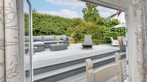 Una terraza con mobiliario exterior, una jardinera de piedra y un seto al fondo.
