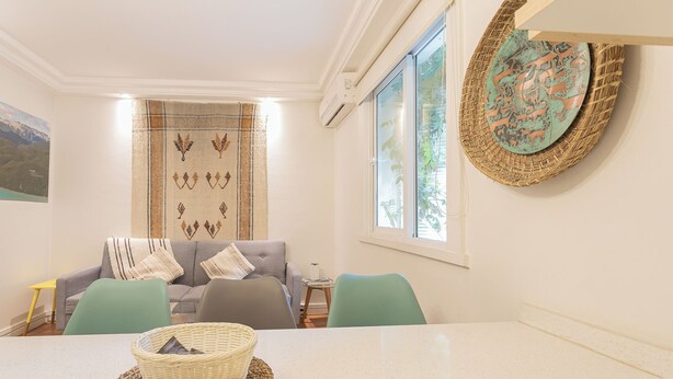 Een woonkamer met een grijze bank, blauwgroene stoelen, een witte tafel en een gevlochten mand.
