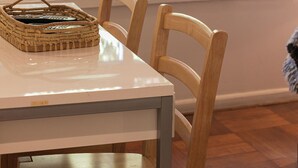 Een eettafel met stoelen, een gevlochten mand en een raam met jaloezieën.