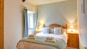 A neatly made bed with pillows and a blanket, a wooden headboard, two bedside tables with lamps, a window with curtains, and a patterned wallpaper. - 2 Bed in Carmel (oc-wai211) (Carmel)