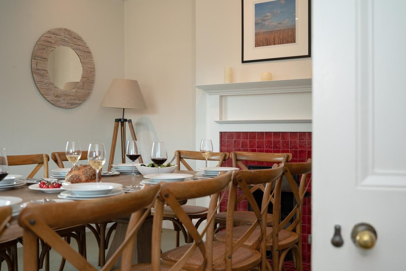 Une salle à manger avec une cheminée, des chaises en bois, un miroir rond et une table mise pour le repas.