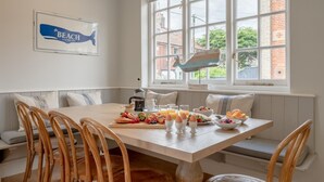 A dining area with a wooden table, chairs, and a breakfast spread. - 7 Bed in Aldeburgh (oc-gbl) (Aldeburgh)
