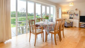Un coin repas avec une table dressée pour quatre personnes, de grandes fenêtres, une bibliothèque et un téléviseur.