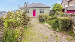 Une maison avec une porte rouge, entourée d’un chemin de gravier et de différentes plantes.