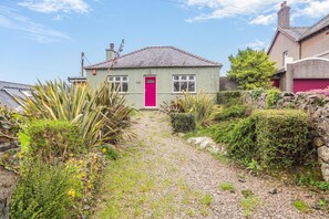A house with a red door, surrounded by a gravel path and various plants. - 3 Bed in Pwllheli (oc-bow04) (Pwllheli)