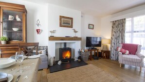 Een gezellige woonkamer met een open haard, een eethoek met een tafel gedekt voor twee personen, en een comfortabele fauteuil.