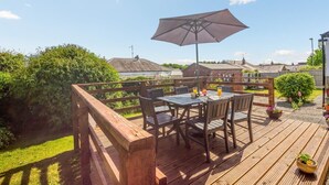 Een houten terras met een tafel, stoelen, een grote parasol en potplanten.