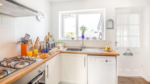 Een moderne keuken met witte kasten, een gasfornuis, een vaatwasser en een raam voor natuurlijk licht.