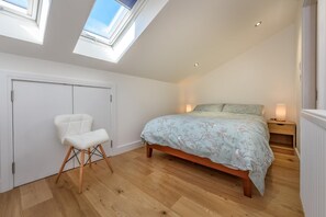 Ein Schlafzimmer mit Dachfenster, einem Bett mit Blumenmuster, einem weißen Stuhl und einem Nachttisch mit Lampe.