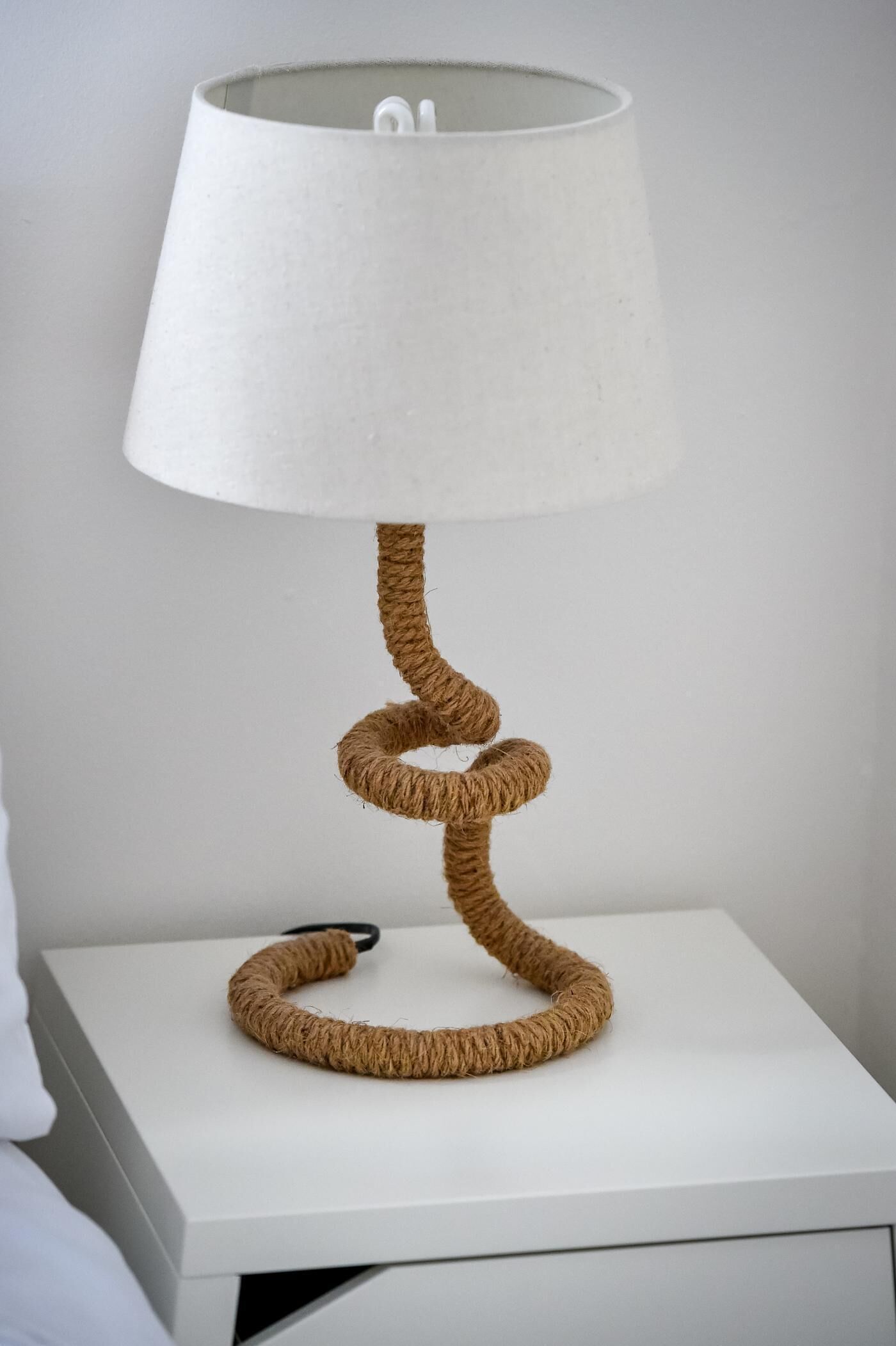 Una mesita de noche blanca con una lámpara original de estilo cuerda.