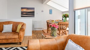 Una sala de estar moderna con un sofá de cuero, una mesa de comedor con sillas y vistas al exterior a través de amplios ventanales.