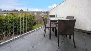 Un balcón con mesa y sillas, vista al jardín y una pared blanca.