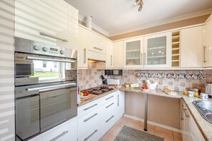 A modern kitchen with stainless steel appliances, white cabinetry, and a breakfast setup. - 4 Bed in Morfa Nefyn (oc-bow10) (Morfa Nefyn)