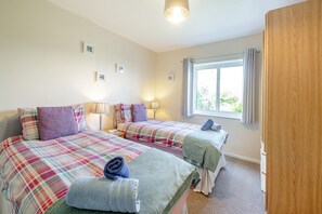 A hotel room with two beds, a window with curtains, a wooden wardrobe, and a carpeted floor. - 4 Bed in Morfa Nefyn (oc-bow10) (Morfa Nefyn)